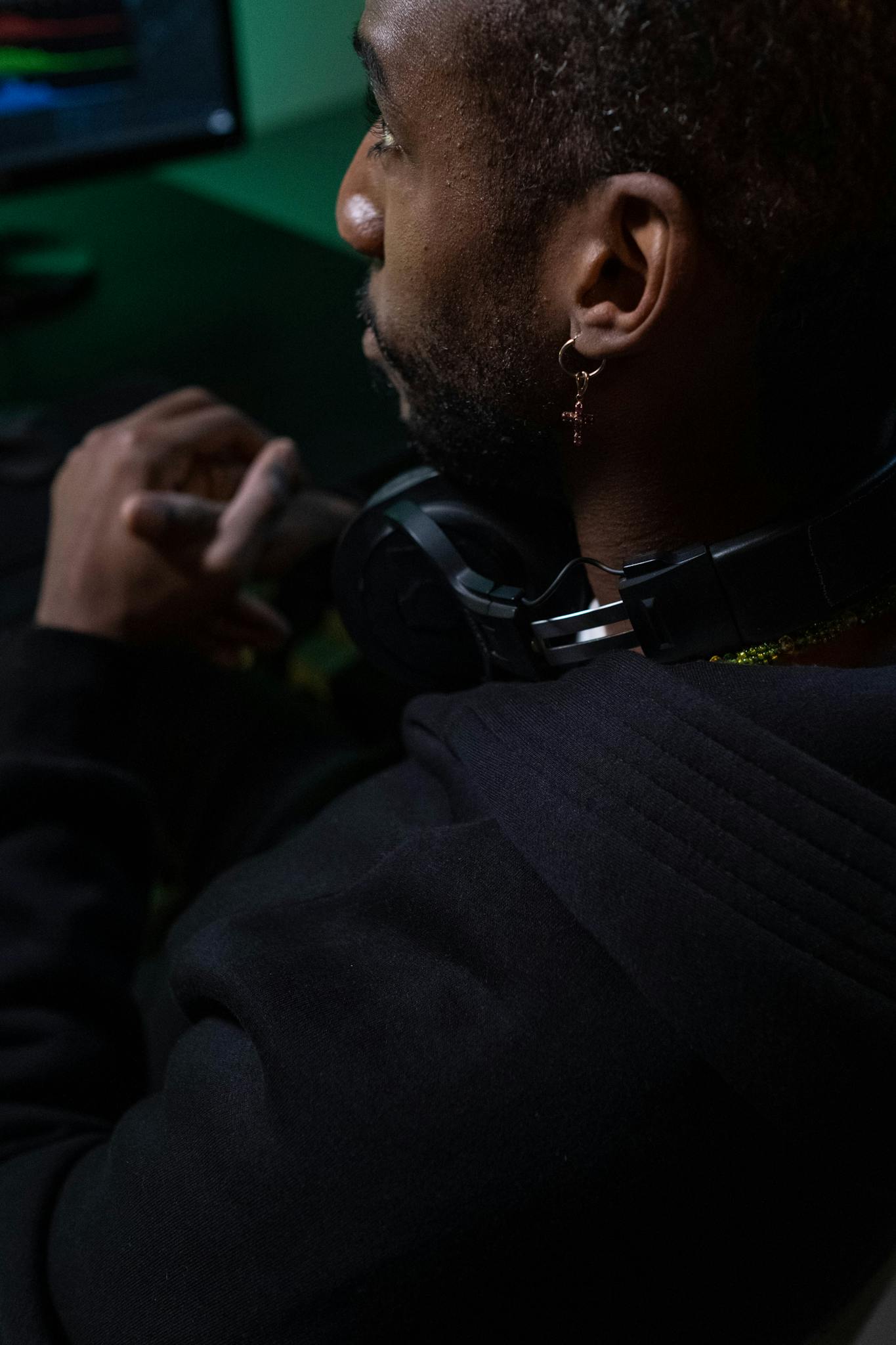 African American man seated with headphones in a dimly lit room, focused on editing tasks.